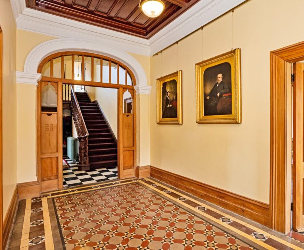 Light yellow walls in the hall with John and Jane photos framed in gold. Wooden stairs to the first floor.