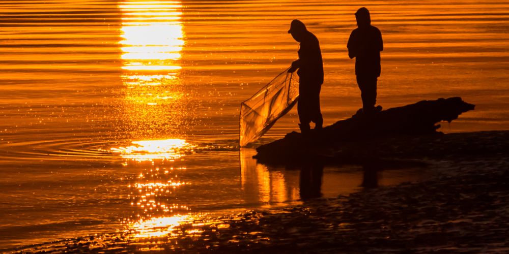 Two persons whitebait fishing in a beautiful orange-golden sunset.